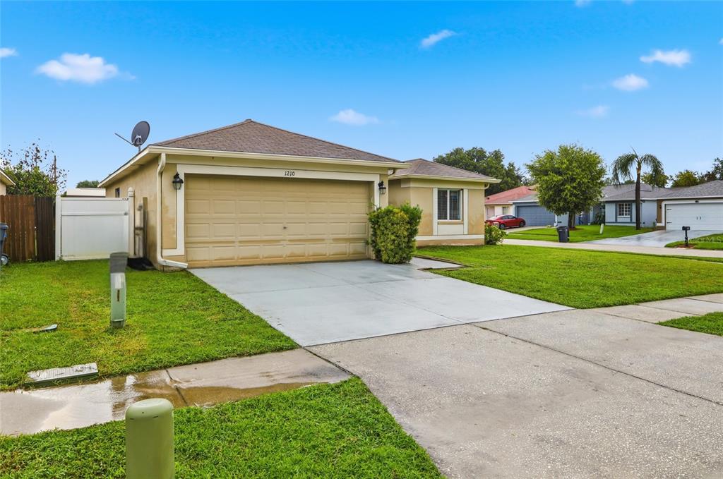 A single-story house with a tan exterior, a two-car garage, and a concrete driveway — 1210 BLUFIELD AVENUE, BRANDON, FL