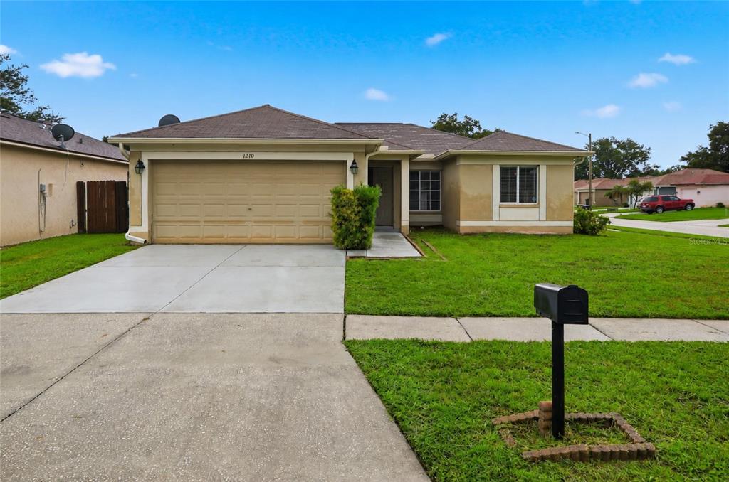 A single-story house with a tan stucco exterior, a two-car garage, and a concrete driveway — 1210 BLUFIELD AVENUE, BRANDON, FL