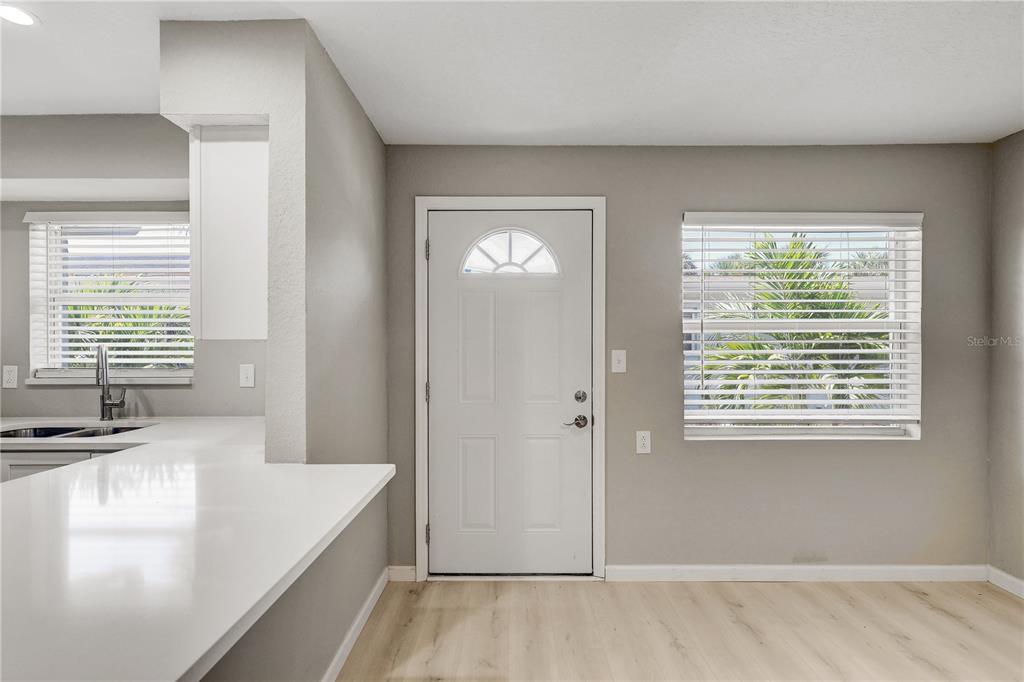 A kitchen and dining area features white countertops, light wood-look flooring, and a white door — 9030 BLIND PASS ROAD UNIT C9, ST PETERSBURG, FL
