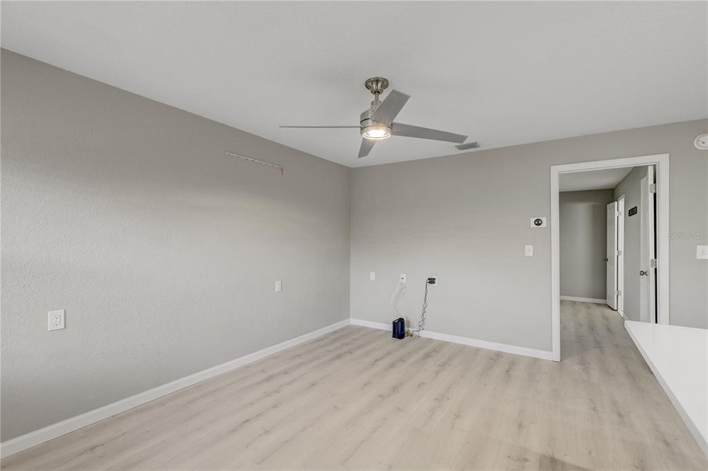 An empty room with light wood-look flooring, gray walls, and a ceiling fan — 9030 BLIND PASS ROAD UNIT C9, ST PETERSBURG, FL