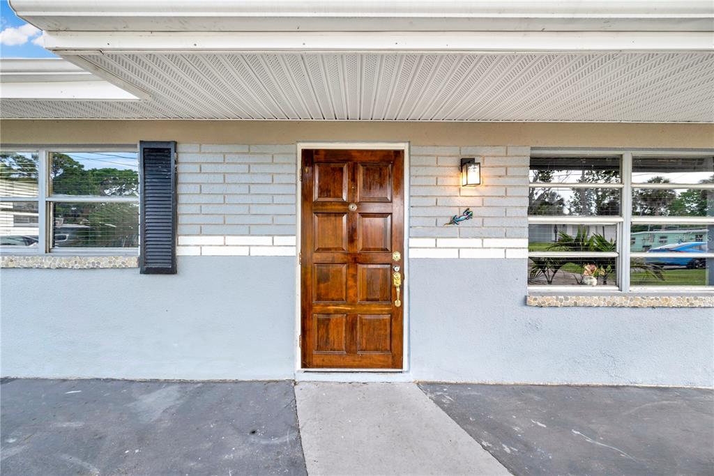 A front exterior view shows a wooden door, gray brick walls, and a concrete porch — 6714 SANDRA DRIVE, PORT RICHEY, FL