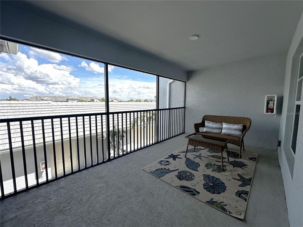 A screened-in balcony features a wicker loveseat, a small table, and a seashell-patterned area rug — 14231 HERITAGE LANDING BOULEVARD UNIT 1928, PUNTA GORDA, FL