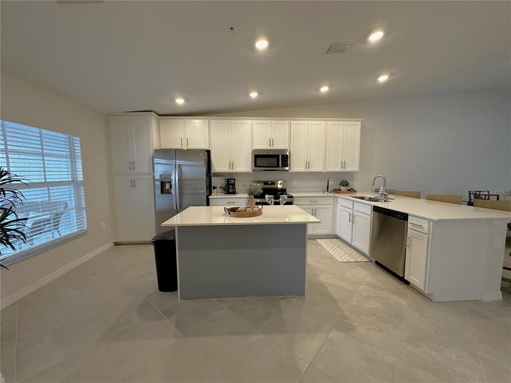 A kitchen features white cabinetry, stainless steel appliances, a central island, and light tile flooring — 14231 HERITAGE LANDING BOULEVARD UNIT 1928, PUNTA GORDA, FL