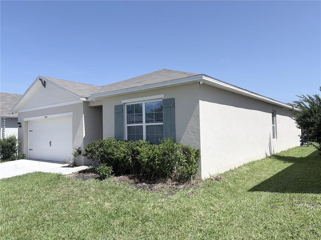 A single-story house with a beige stucco exterior, a two-car garage, and blue window shutters — 1270 IGUANA LOOP, DAVENPORT, FL