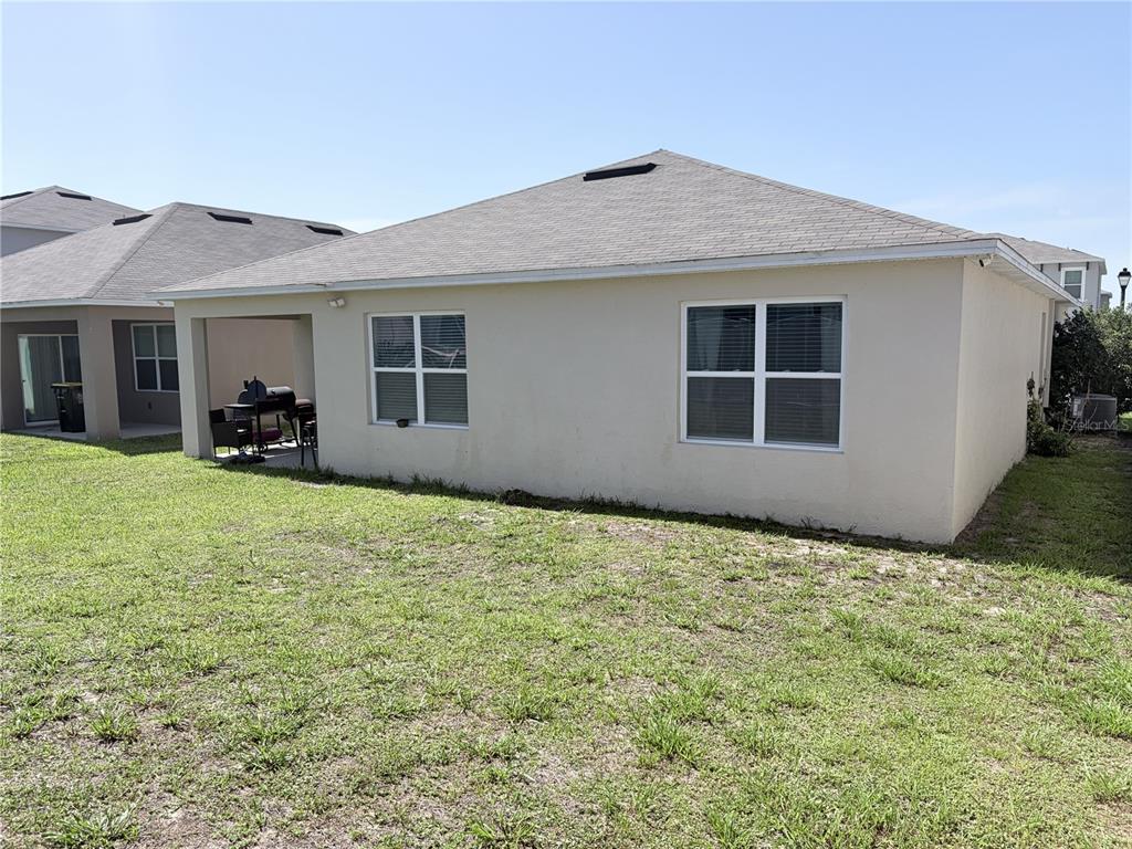 The exterior rear view of a beige house features a covered patio and a lawn — 1270 IGUANA LOOP, DAVENPORT, FL