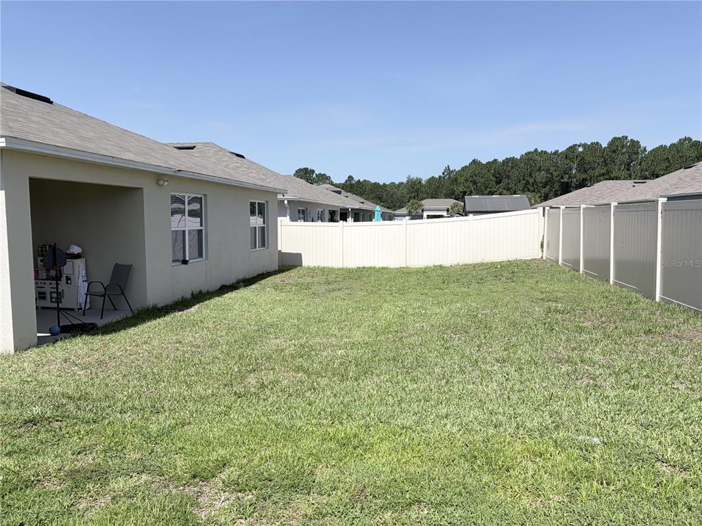 A backyard with a covered patio, a tan house, and a white vinyl privacy fence — 1270 IGUANA LOOP, DAVENPORT, FL