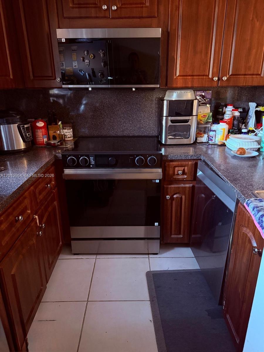 A kitchen features wooden cabinets, stainless steel appliances, and dark countertops over tiled flooring — 1250 NE 125th St # 317A, North Miami FL 33161, NORTH MIAMI, FL