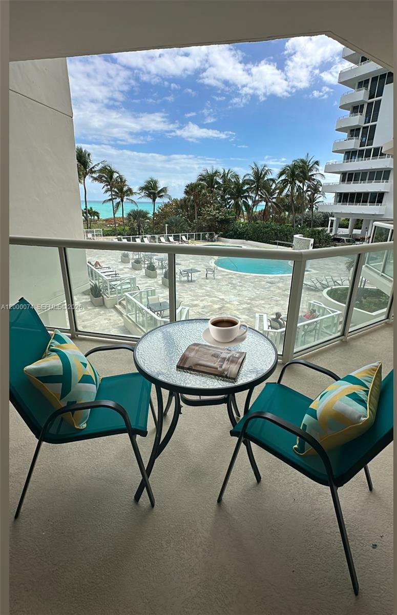 A balcony with a small table and two chairs overlooks a swimming pool and ocean — 8925 Collins Ave # 2J, Surfside FL 33154, SURFSIDE, FL