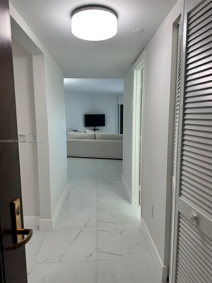 A hallway with white marble-look tile flooring leads to a living area with a sofa — 8925 Collins Ave # 2J, Surfside FL 33154, SURFSIDE, FL