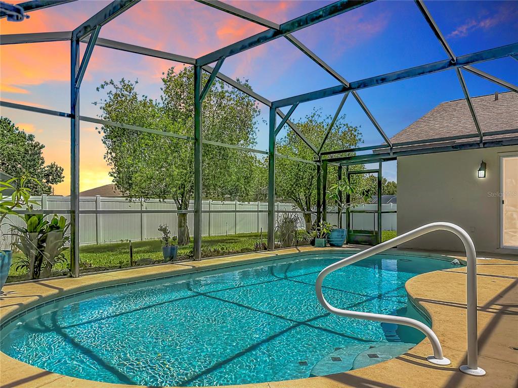 A screened-in swimming pool with a white fence and sunset sky in the background — 8654 ALEGRE CIRCLE, ORLANDO, FL