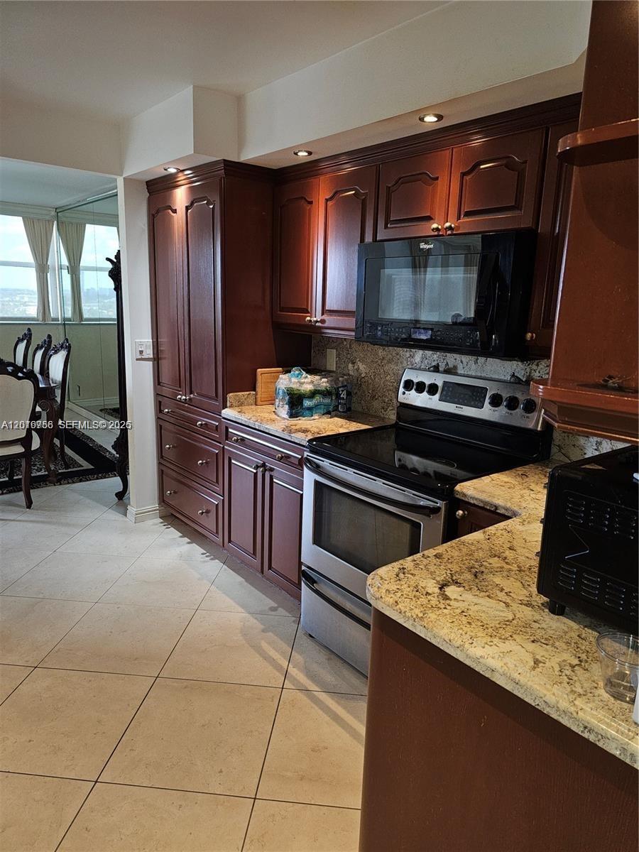 A kitchen features dark wood cabinets, granite countertops, stainless steel appliances, and tile flooring — 2049 S Ocean Dr, Hallandale Beach FL 33009, HALLANDALE BEACH, FL
