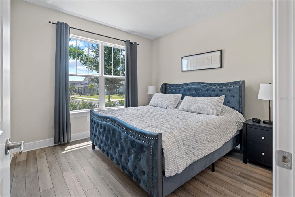 A bedroom features a tufted blue bed, wood-look flooring, and a window with gray curtains — 15203 WILLOW RIDGE DRIVE, MONTVERDE, FL