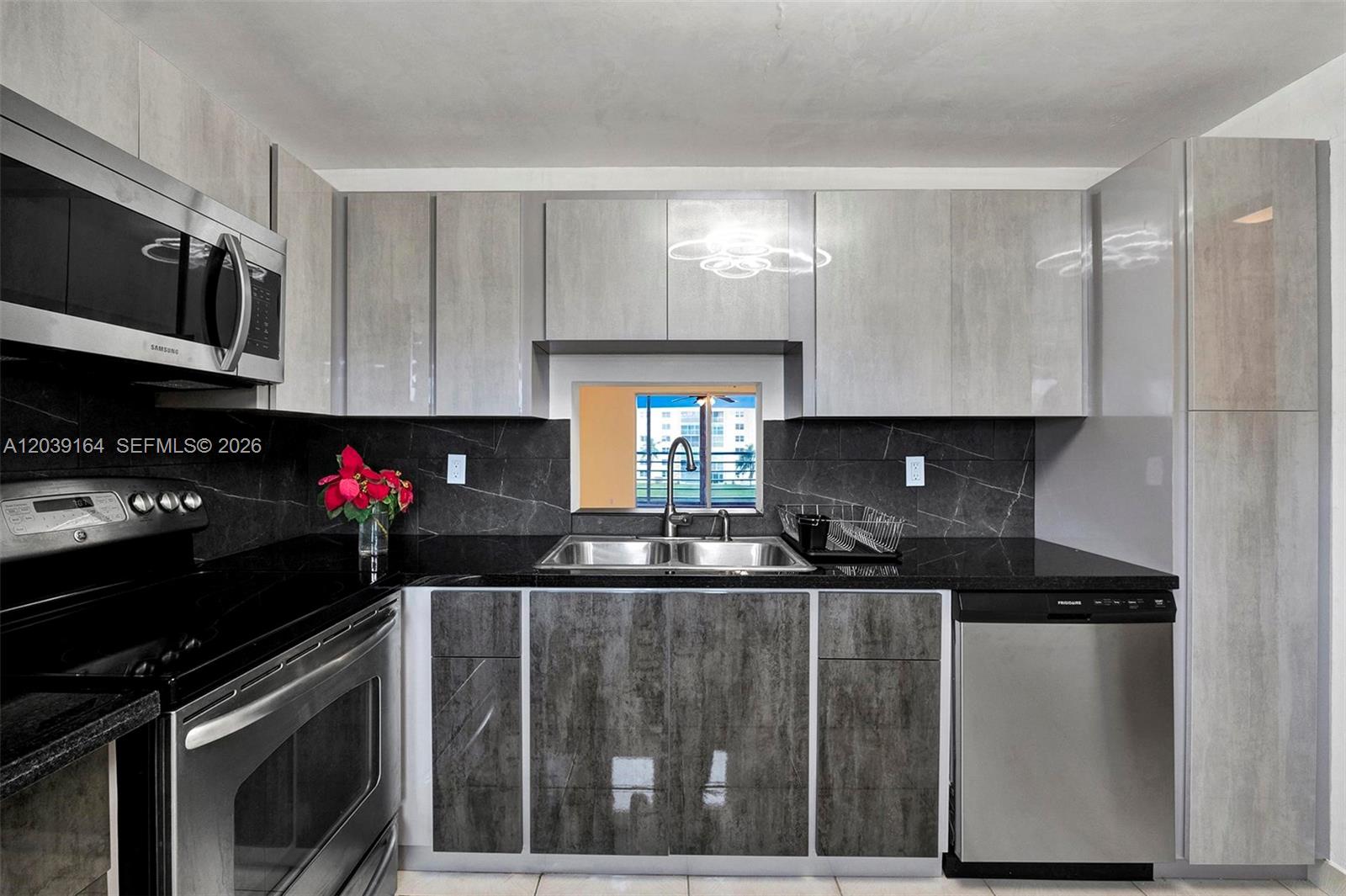 A modern kitchen features gray cabinets, black countertops, stainless steel appliances, and a pass-through window — 431 SE 3rd St # 402, Dania Beach FL 33004, DANIA BEACH, FL