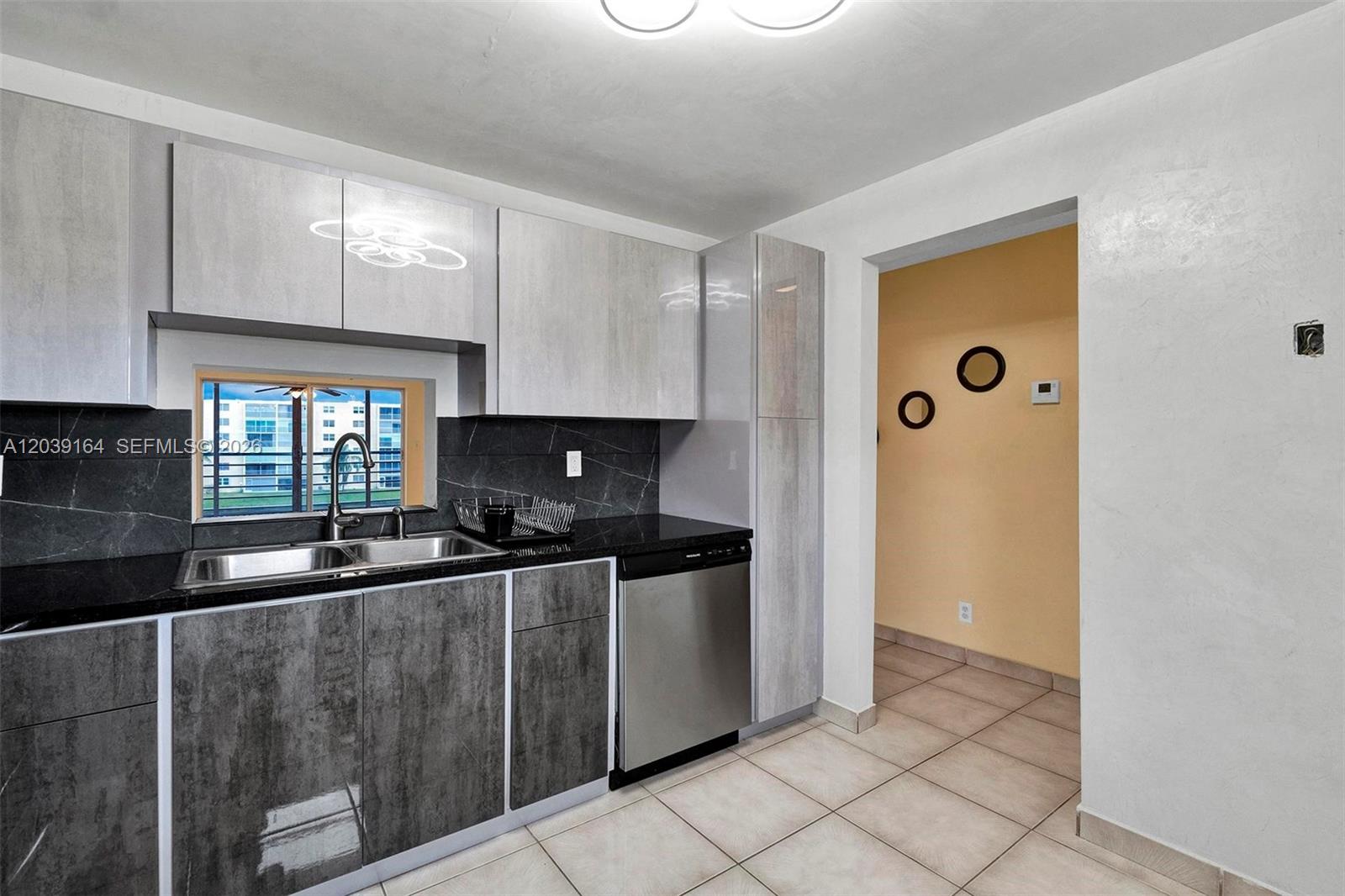 A kitchen features grey and white cabinetry, black countertops, a stainless steel dishwasher, and tile flooring — 431 SE 3rd St # 402, Dania Beach FL 33004, DANIA BEACH, FL