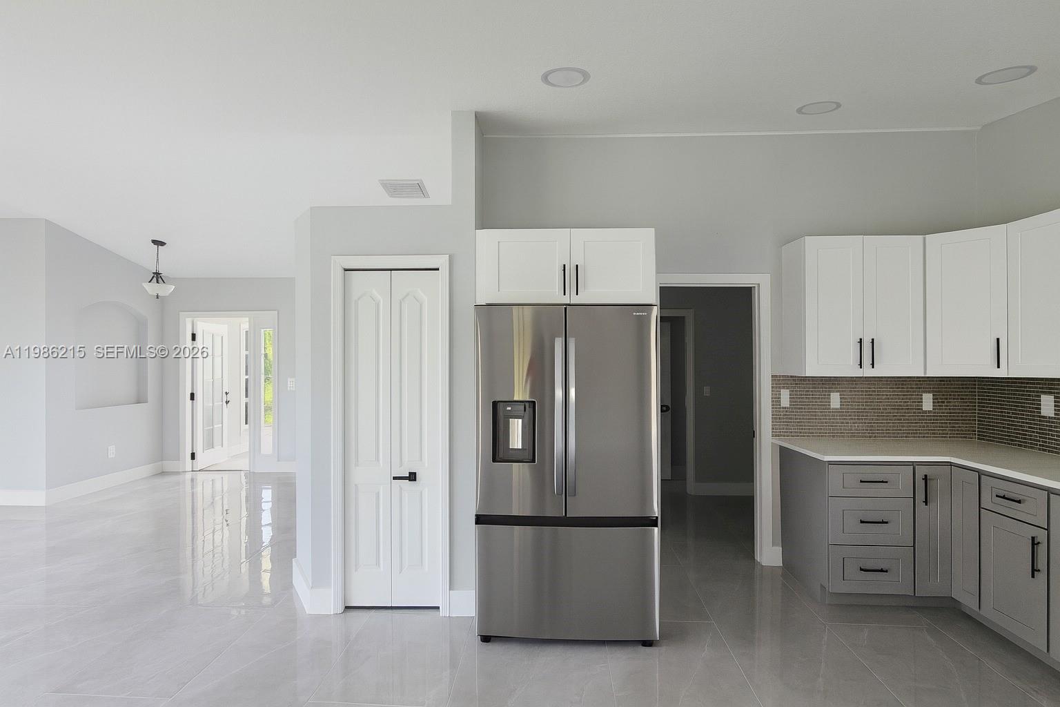 A modern kitchen features gray lower cabinets, white upper cabinets, and a stainless steel refrigerator — 116 ridgemont Dr, Lehigh Acres FL 33972, LEHIGH ACRES, FL