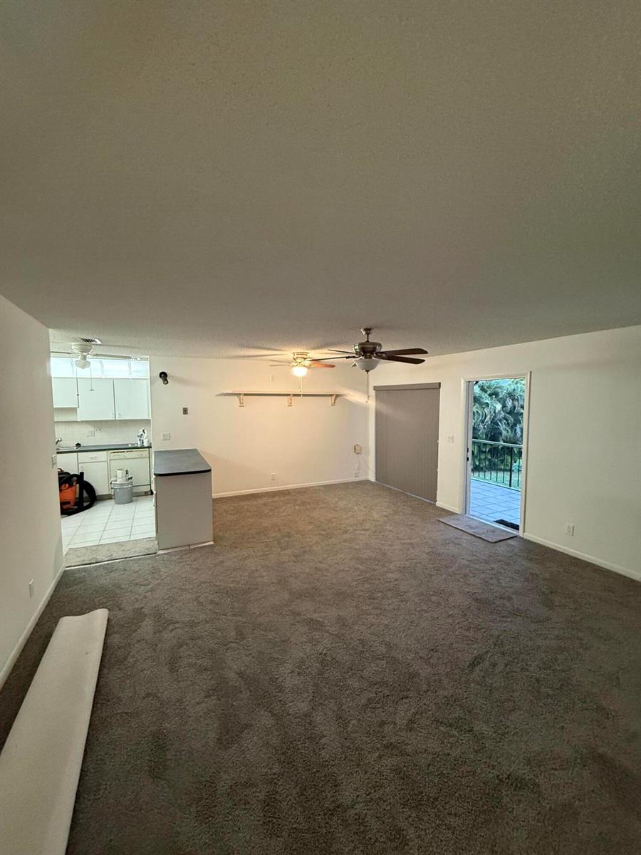 A living room with gray carpet, a ceiling fan, and an adjacent kitchen area — 5795 La Pinata Boulevard # 2, FL 33463, FL