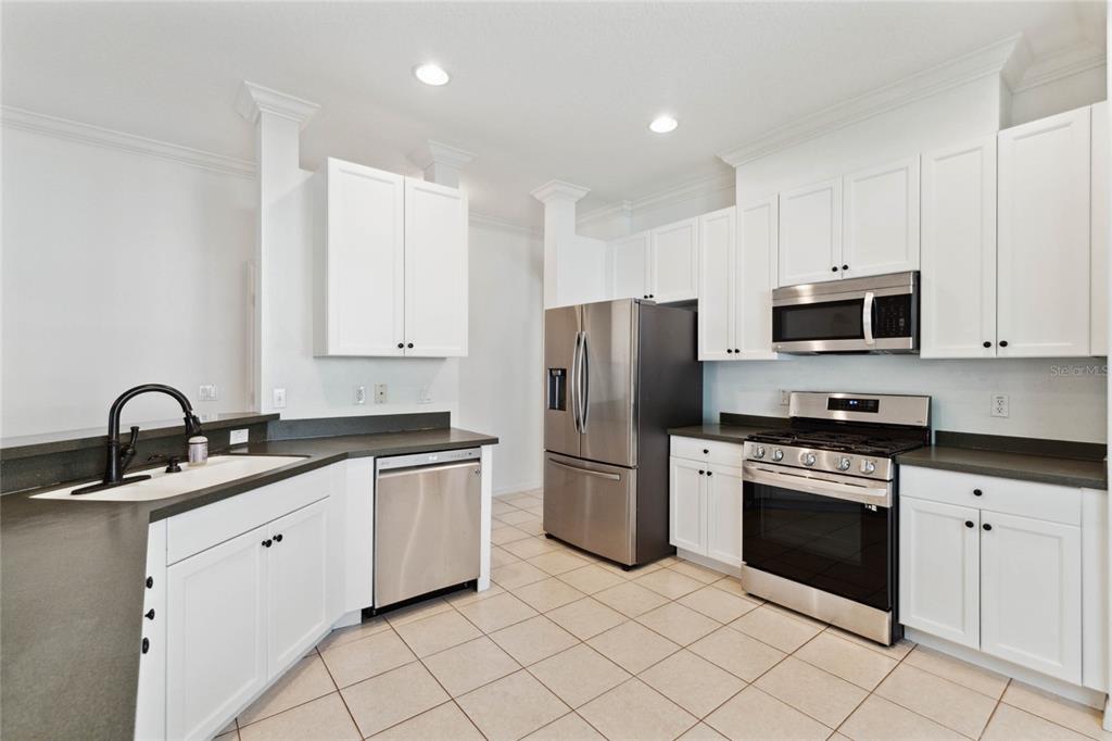 A kitchen with white cabinets, stainless steel appliances, and dark countertops on a tiled floor — 5007 RIVER GEM AVENUE, WINDERMERE, FL