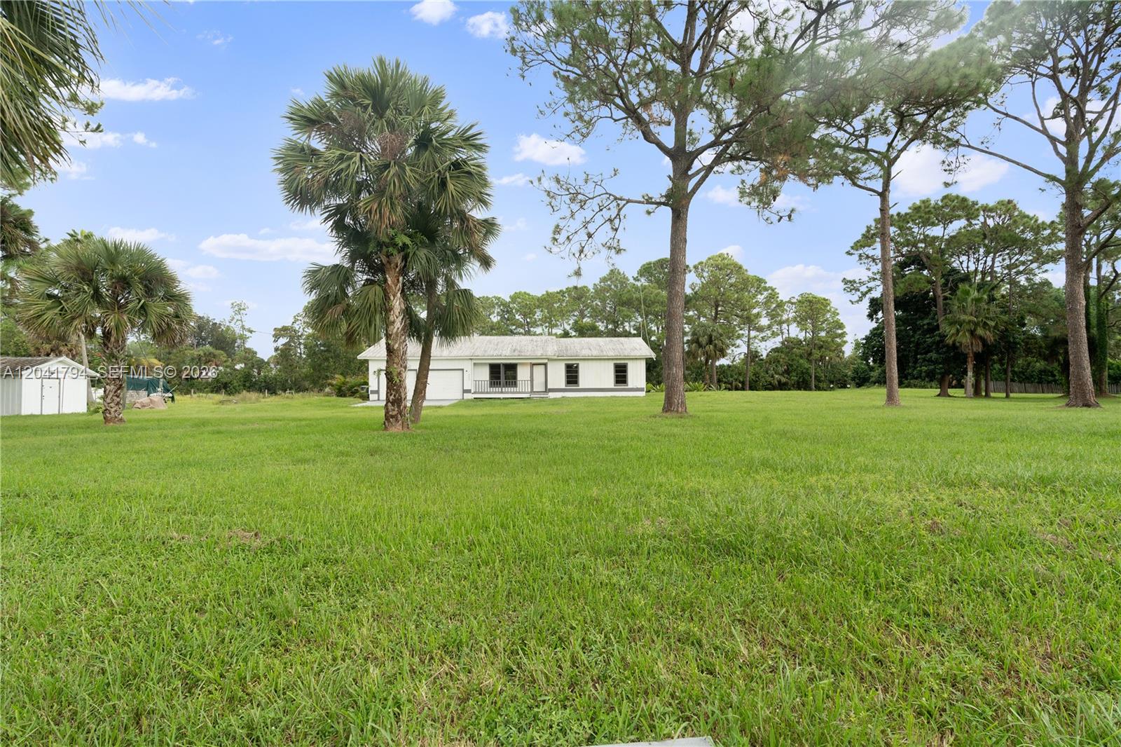 A single-story white house sits on a large, grassy lot with several palm and pine trees — 9949 N 154th Rd N, Jupiter FL 33478, JUPITER, FL