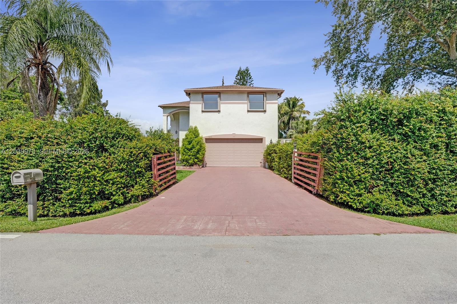 A two-story house with a beige exterior and a paved driveway sits behind tall hedges — 2151 NW 121st Ave, Plantation FL 33323, PLANTATION, FL