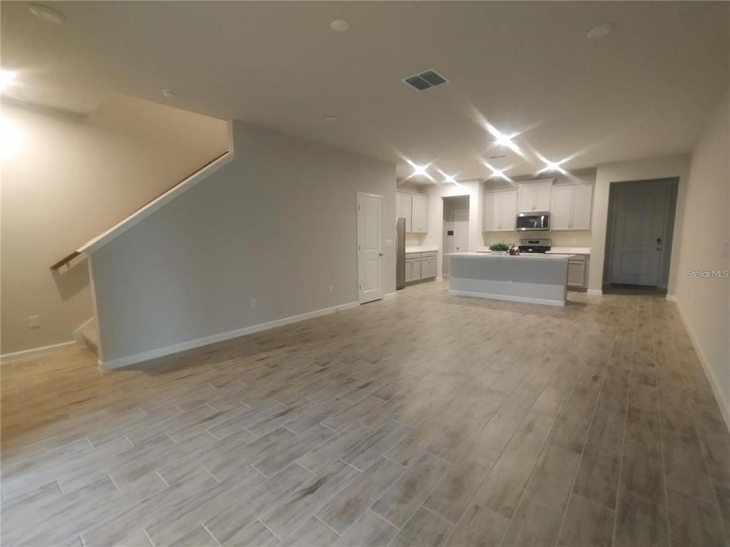 An open-concept living area features light wood-look tile flooring, a staircase, and a modern kitchen — 26010 WOVEN WICKER BEND, LUTZ, FL