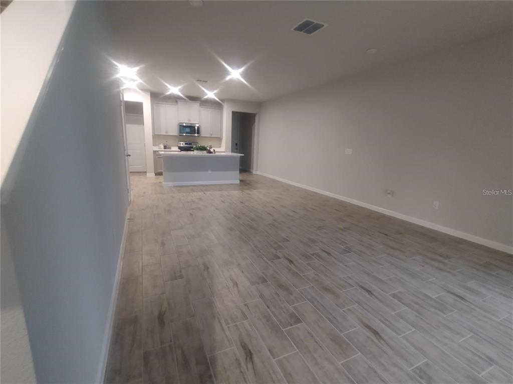An open-concept living area features light wood-look tile flooring and a kitchen with white cabinetry — 26010 WOVEN WICKER BEND, LUTZ, FL