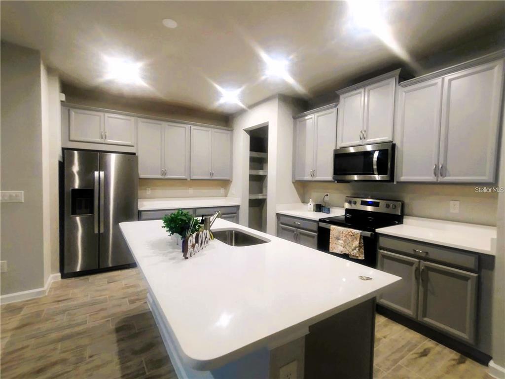 A kitchen features gray cabinets, white countertops, a center island, and stainless steel appliances — 26010 WOVEN WICKER BEND, LUTZ, FL