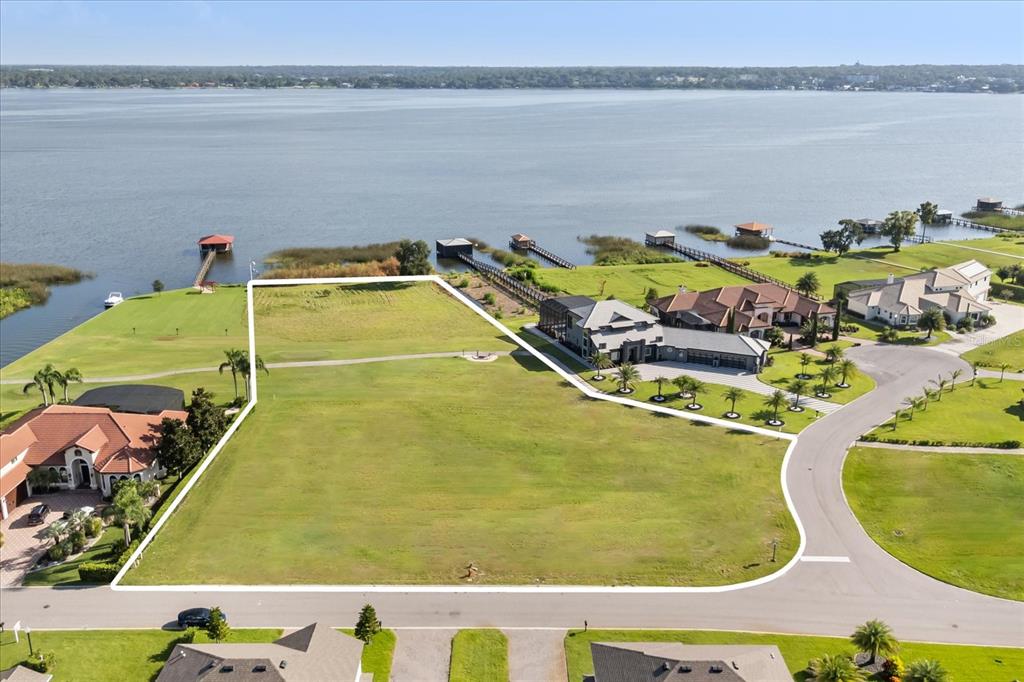 An aerial view shows a vacant, grassy waterfront lot bordered by residential homes and docks — 29901 OSPREY COURT, TAVARES, FL
