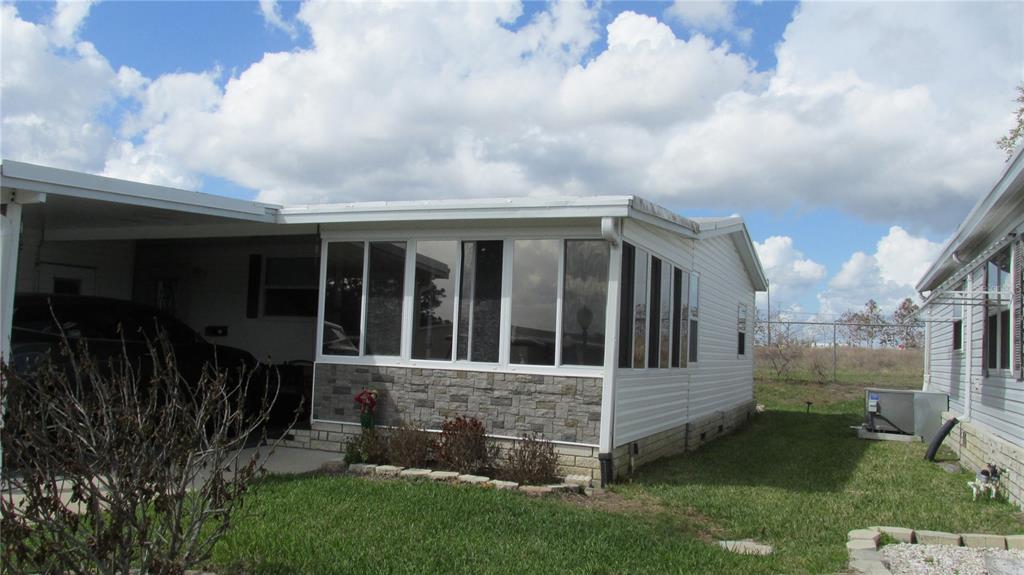 A mobile home exterior features a stone-accented sunroom, a carport, and a grassy yard — 33 EDINBURGH DRIVE, HAINES CITY, FL