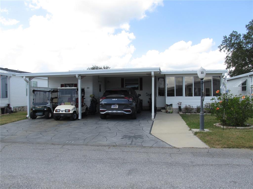A single-story manufactured home with a carport, driveway, golf carts, and a front walkway — 33 EDINBURGH DRIVE, HAINES CITY, FL