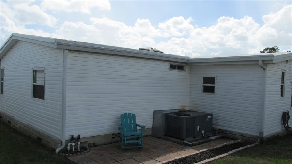 The exterior of a white vinyl-sided house features a small patio, an air conditioning unit, and a chair — 33 EDINBURGH DRIVE, HAINES CITY, FL