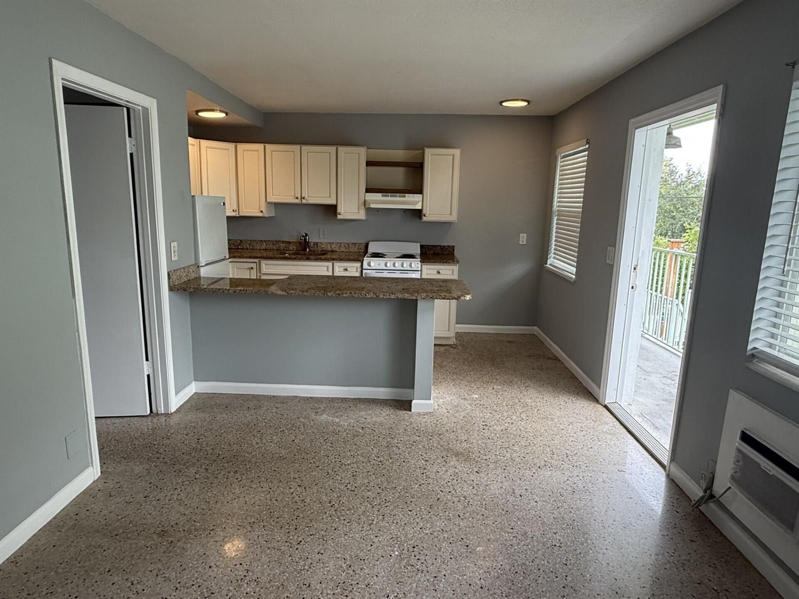 A kitchen with granite countertops, white cabinets, and terrazzo flooring opens to a balcony — 1118 N H Street # 15, FL 33460, FL