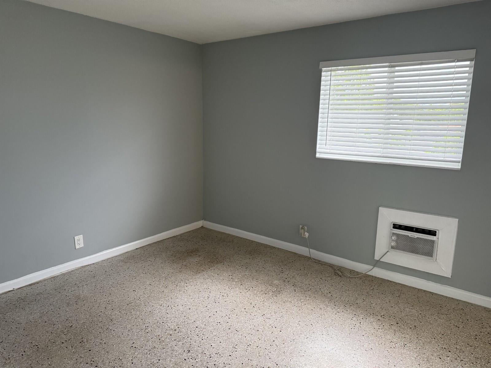 A room with gray walls, a speckled floor, a window with blinds, and an air conditioner — 1118 N H Street # 15, FL 33460, FL