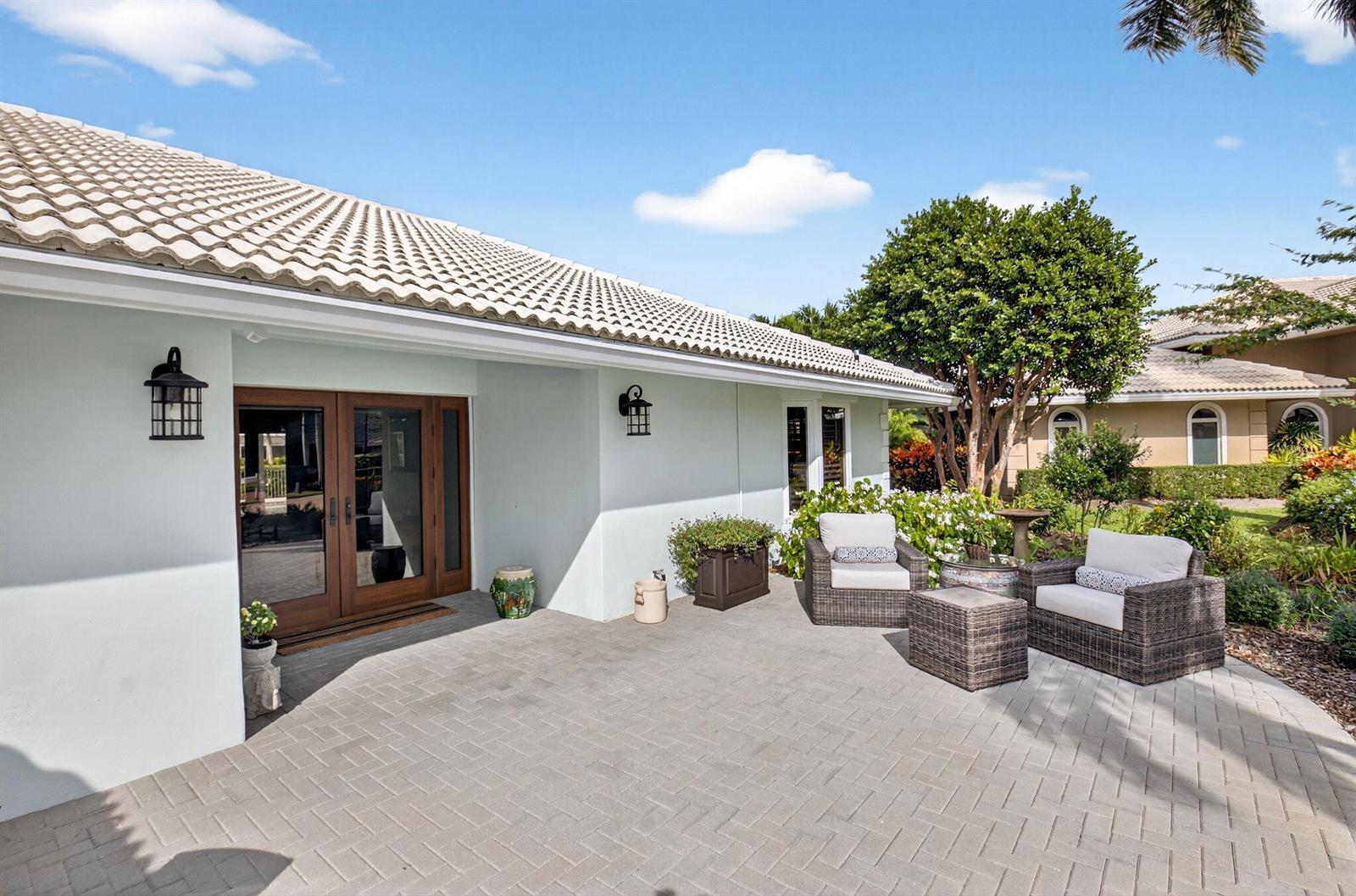 A paved patio features two wicker chairs, a small table, and a double-door entrance — 11949 Date Palm Drive, Boynton Beach FL 33436, BOYNTON BEACH, FL