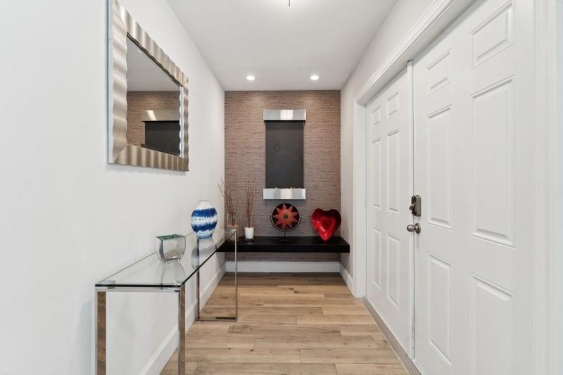 A modern entryway features a glass console table, a wall-mounted water feature, and wood flooring — 13 Little Harbor Way, Deerfield Beach FL 33441, DEERFIELD BEACH, FL