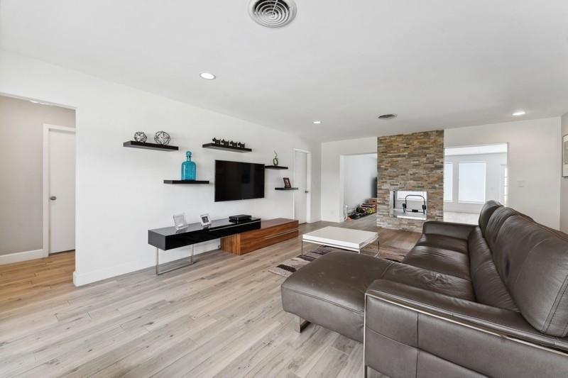 A living room features a stone fireplace, floating shelves, a television, and a leather sectional — 13 Little Harbor Way, Deerfield Beach FL 33441, DEERFIELD BEACH, FL