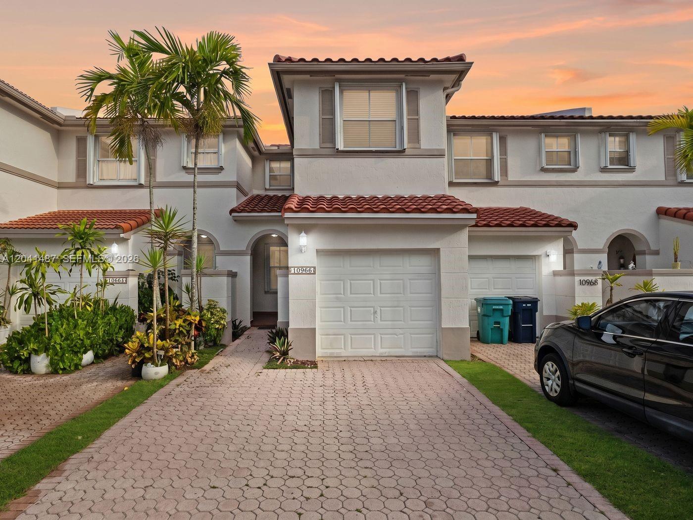 A two-story townhouse with a paved driveway, a garage, and a tiled roof at sunset — 10966 NW 43rd Ter # 10966, Doral FL 33178, DORAL, FL