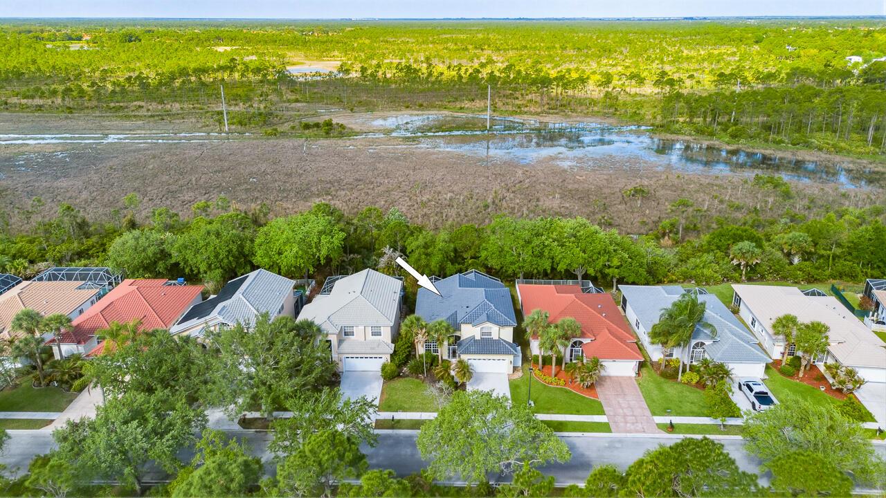 An aerial view shows a suburban neighborhood with houses bordering a large, grassy wetland area — 7213 SE Magellan Lane, Stuart FL 34997, STUART, FL