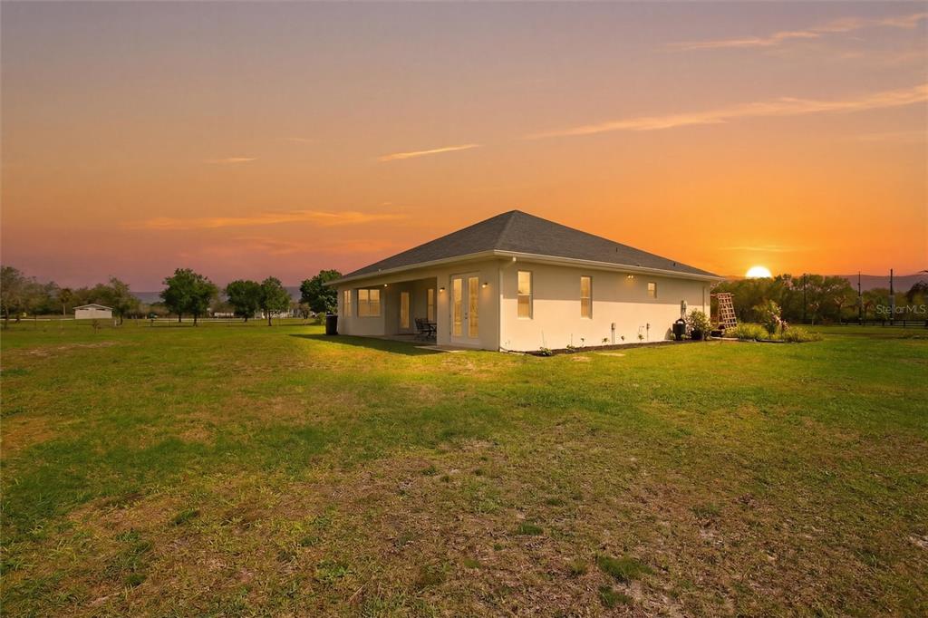 A single-story house with a covered patio sits in a large grassy field at sunset — 10080 WAUCHULA ROAD, MYAKKA CITY, FL