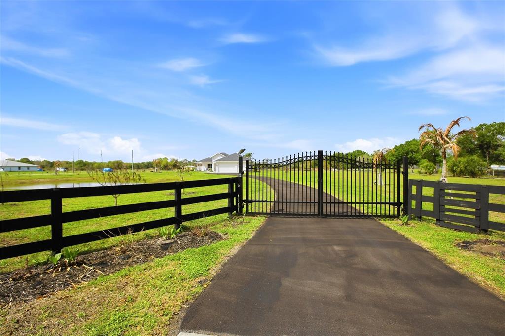 A black metal gate opens onto a paved driveway leading to a house on a lawn — 10080 WAUCHULA ROAD, MYAKKA CITY, FL