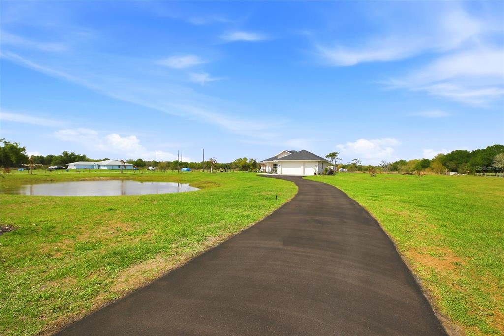 A paved driveway leads to a house with a pond on a grassy lot — 10080 WAUCHULA ROAD, MYAKKA CITY, FL