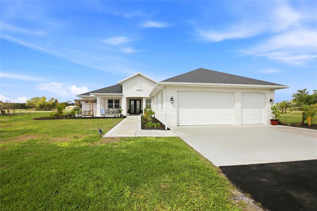 A white single-story house with a three-car garage sits on a large grassy lot — 10080 WAUCHULA ROAD, MYAKKA CITY, FL