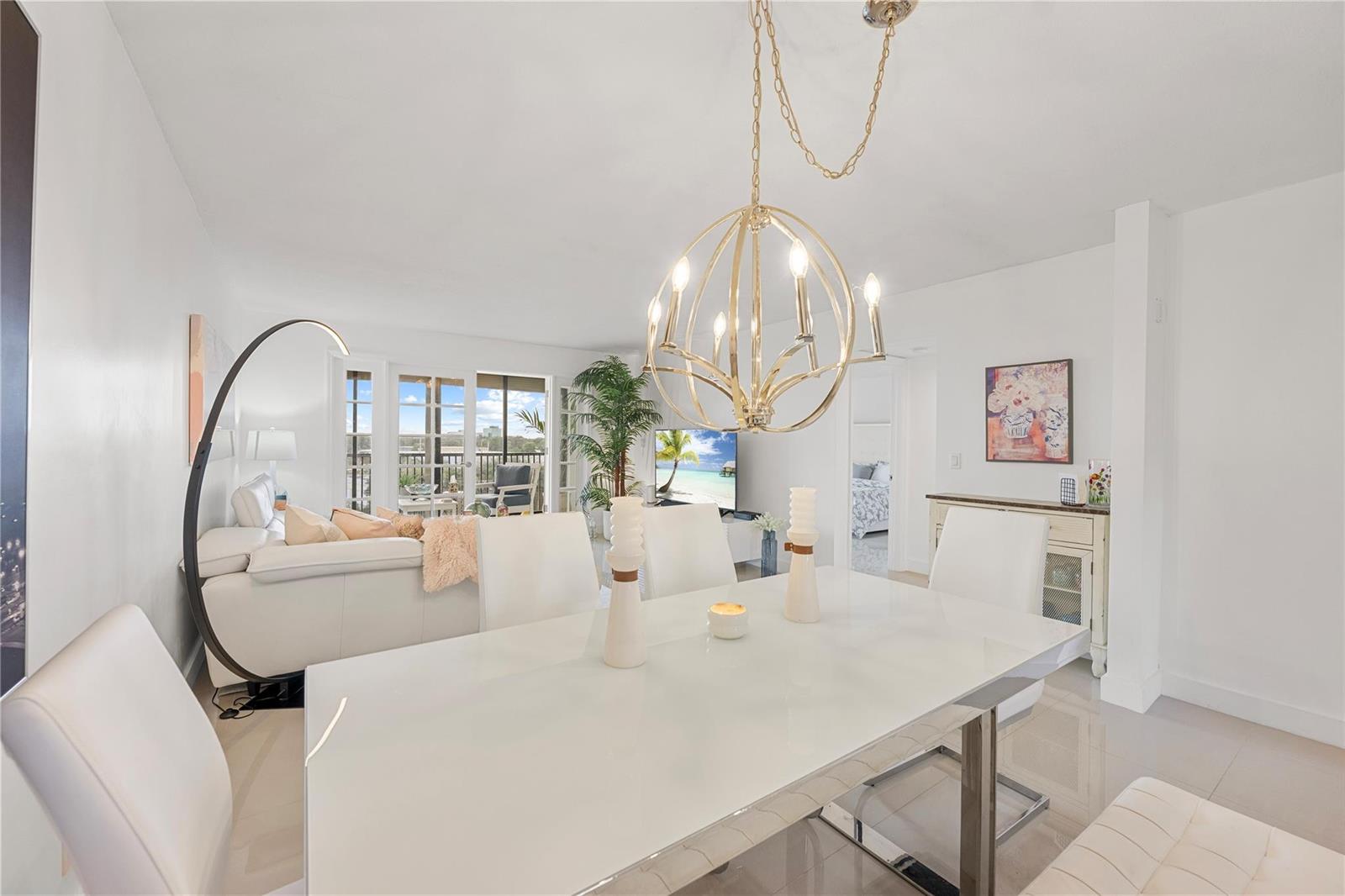 A bright dining area features a white table, modern chandelier, and an adjacent living space — 2202 S Cypress Bend Drive # 606, Pompano Beach FL 33069, POMPANO BEACH, FL