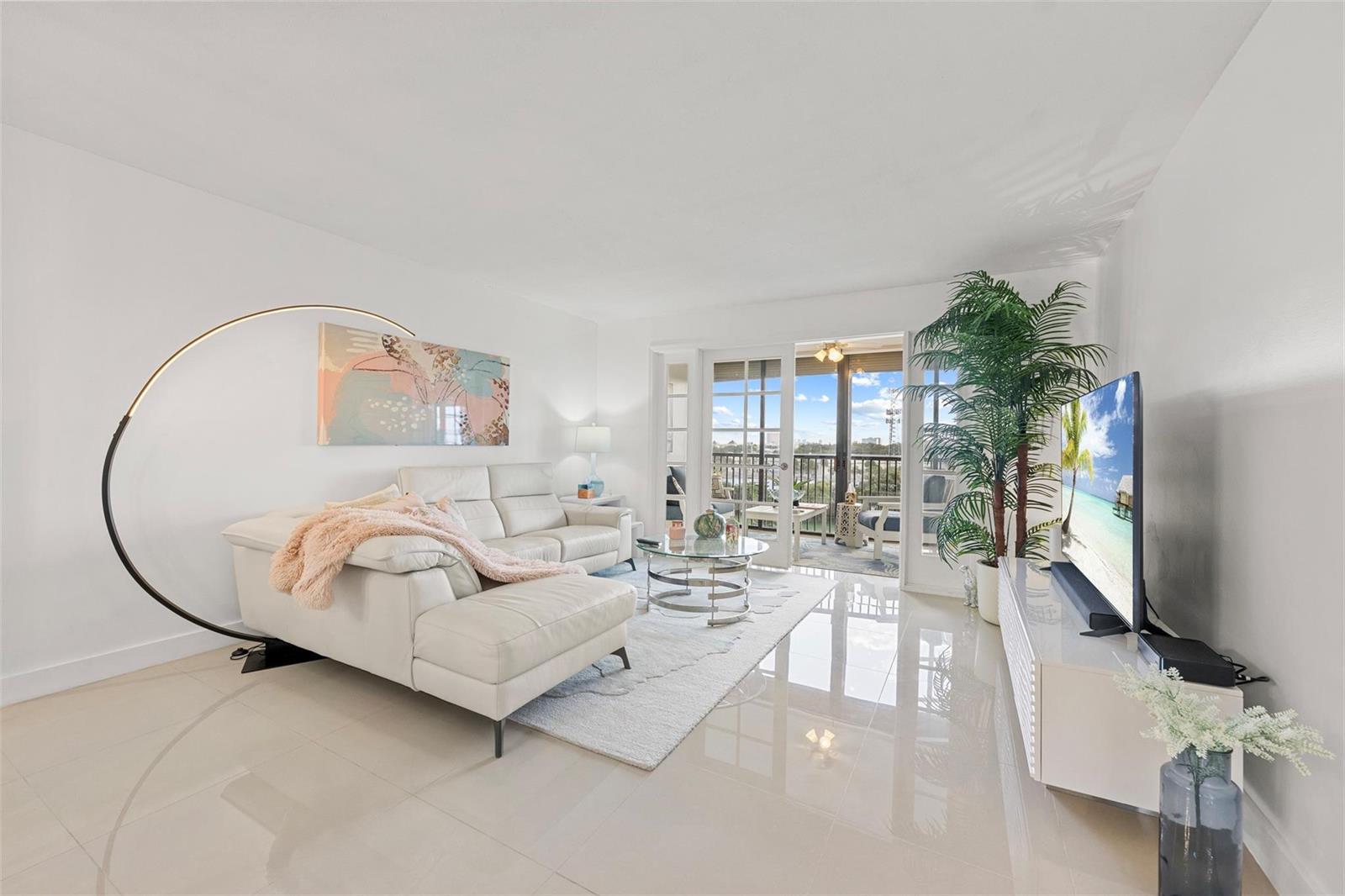 A bright living room features white tile floors, a sectional sofa, and a balcony view — 2202 S Cypress Bend Drive # 606, Pompano Beach FL 33069, POMPANO BEACH, FL