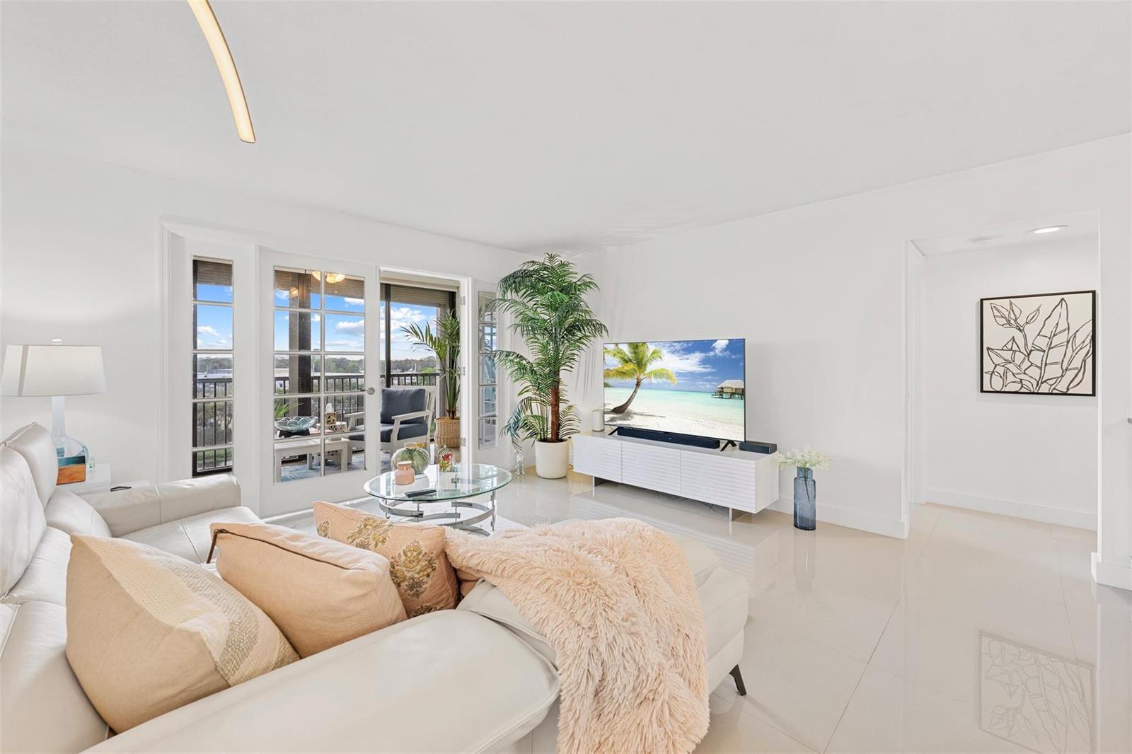 A bright living room features a white sectional sofa, glass coffee table, and balcony access — 2202 S Cypress Bend Drive # 606, Pompano Beach FL 33069, POMPANO BEACH, FL