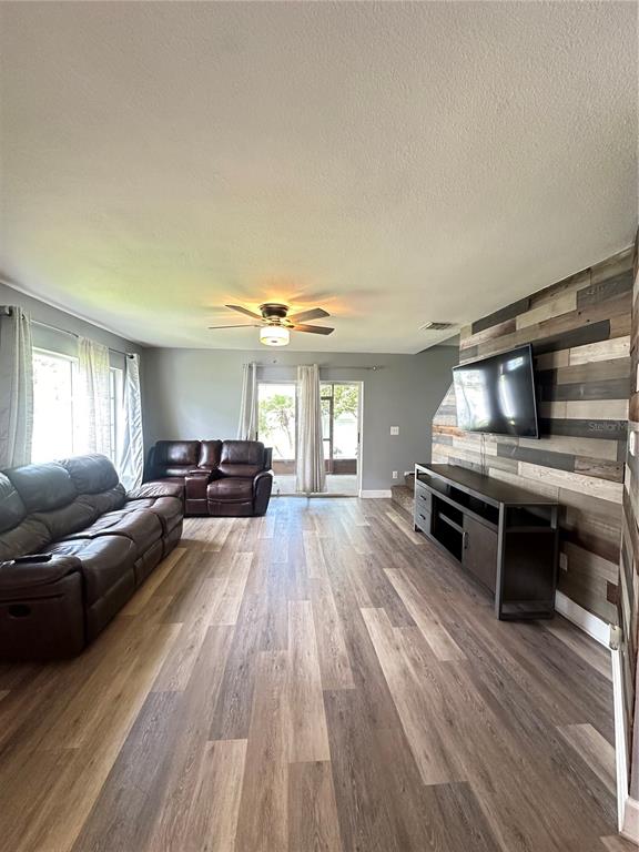 A living room features wood-look flooring, a leather sofa, and a wood-paneled accent wall — 2235 FLUORSHIRE DR DRIVE, BRANDON, FL