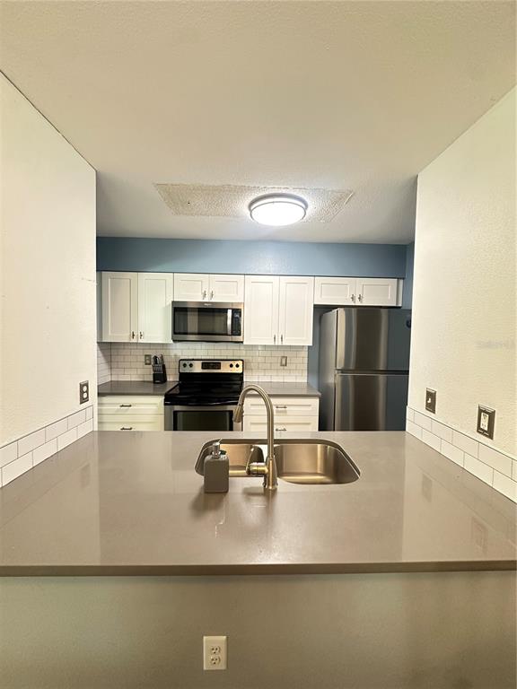 A kitchen features white cabinets, stainless steel appliances, a gray countertop, and a sink island — 2235 FLUORSHIRE DR DRIVE, BRANDON, FL