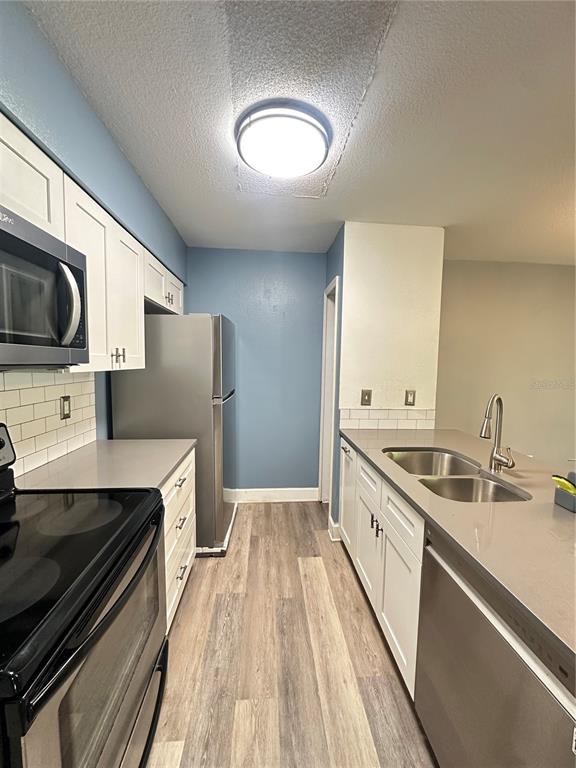 A galley kitchen features white cabinets, stainless steel appliances, gray countertops, and wood-look flooring — 2235 FLUORSHIRE DR DRIVE, BRANDON, FL