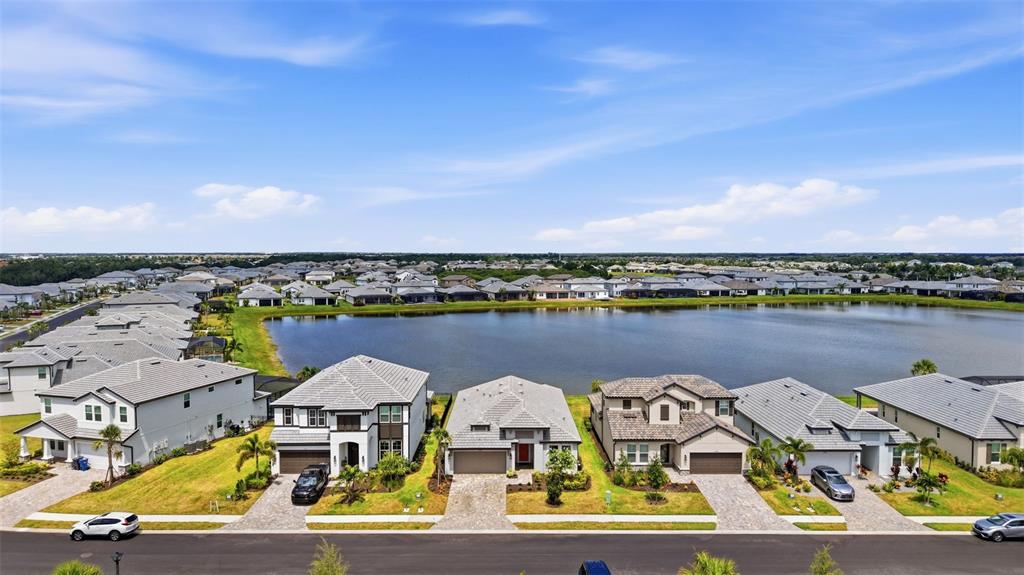An aerial view shows a row of suburban houses facing a lake under a blue sky — 17325 SAVORY MIST CIRCLE, BRADENTON, FL