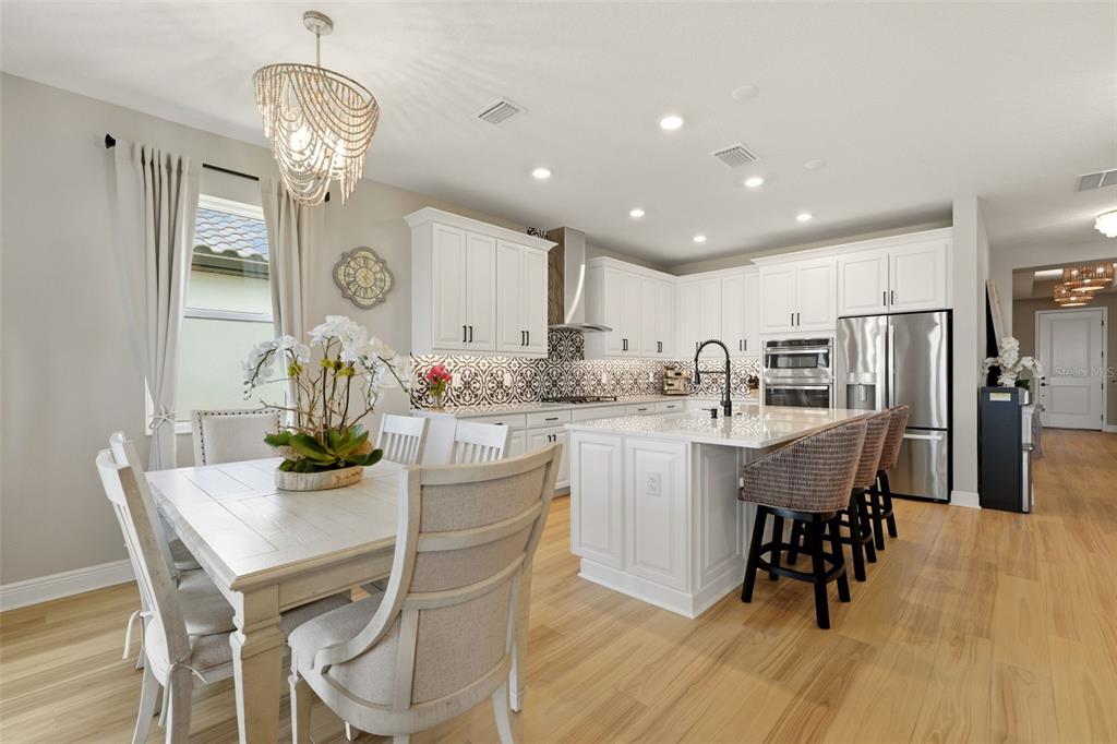A bright kitchen features white cabinetry, a patterned backsplash, a center island, and dining area — 17325 SAVORY MIST CIRCLE, BRADENTON, FL