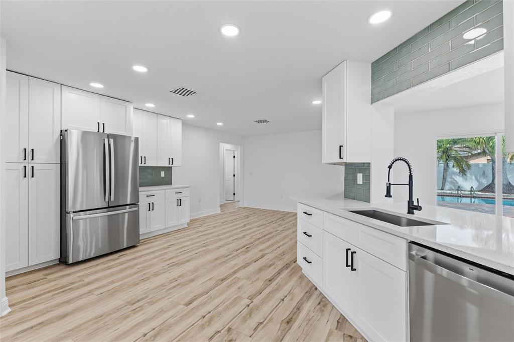 A modern kitchen features white cabinetry, stainless steel appliances, quartz countertops, and light wood flooring — 9354 119TH WAY, SEMINOLE, FL